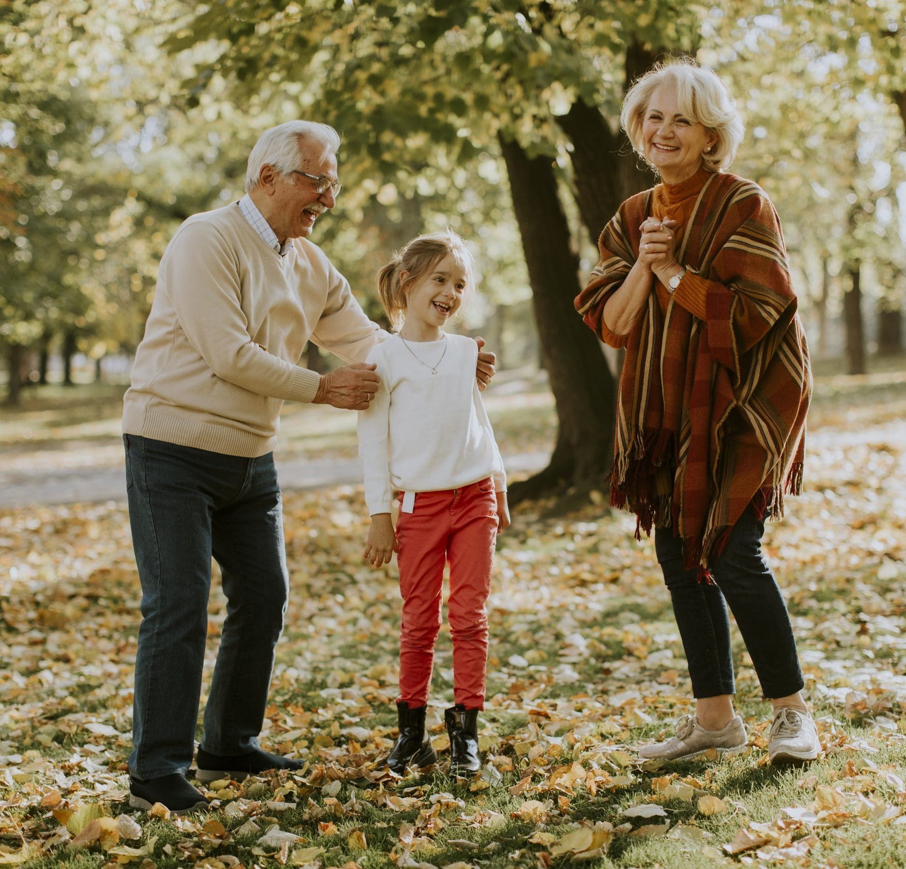 Grandparents playing with their young granddaughter among fallen leaves in a park