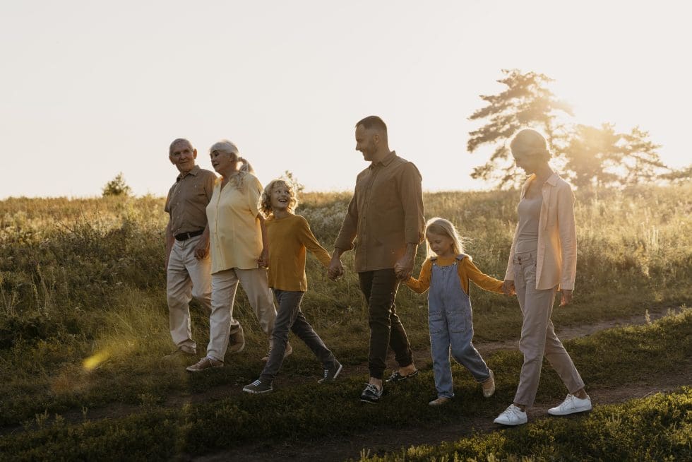 Three generations of a family walking together through a sunlit field at golden hour
