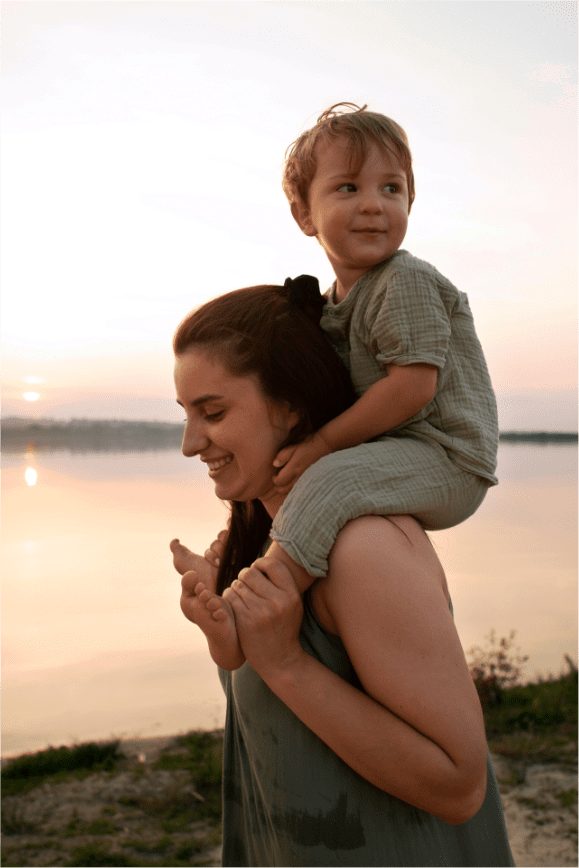 A mother carrying her young son on her shoulders at the shore